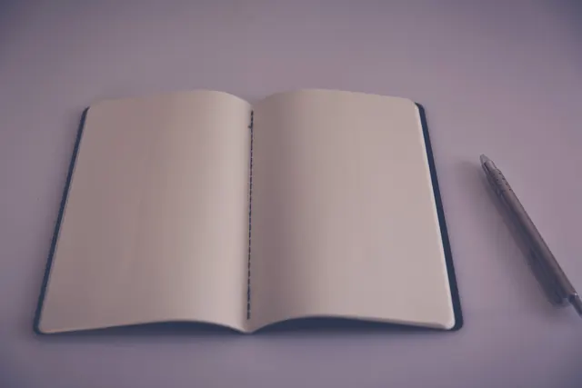 Carnet ouvert sur une page blanche, un stylo posé à côté