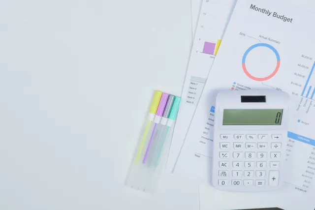 Calculatrice posée sur des documents de budget mensuel, sur un bureau blanc