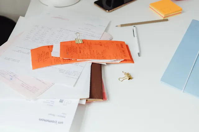Reçus, factures et documents comptables empilés sur un bureau blanc