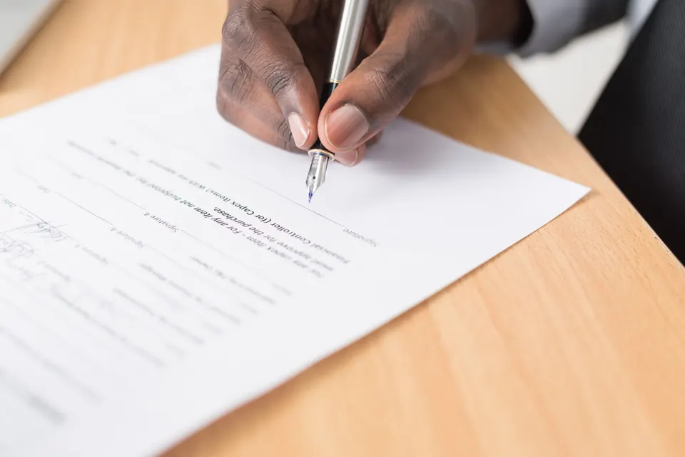 Main signant un devis au stylo sur un bureau en bois