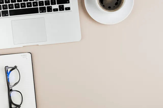 Bureau épuré avec un ordinateur portable, un carnet, des lunettes et un café